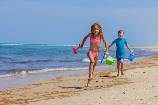 Children have fun run along sandy beach carrying colorful toys