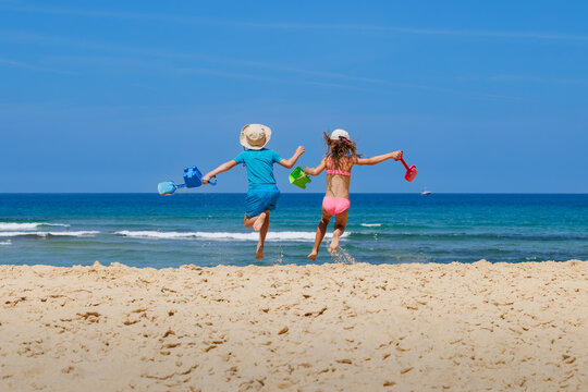 Happy beachgoers leap across sandy beach toward ocean with toys