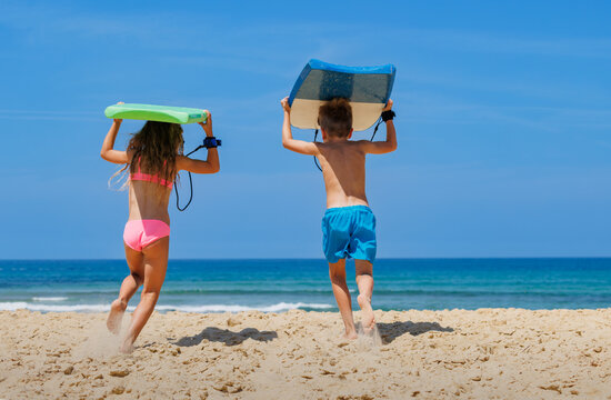 Children carrying bodyboards toward ocean beach under blue sky
