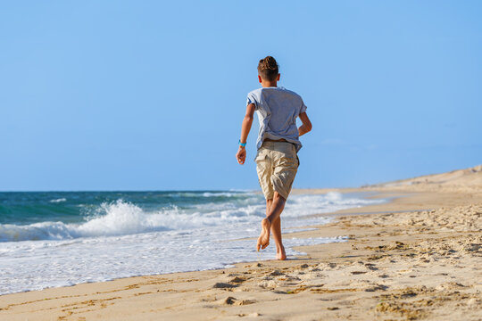 Teenager walking barefoot along sandy beach beside ocean waves