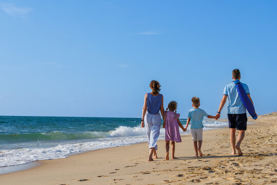 Parents and kids walking barefoot along a sunny beach shoreline