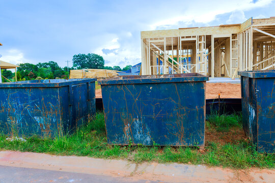 Dumpsters stand near construction site where wooden frames are being built work is ongoing.