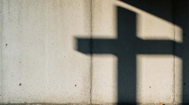 Sunlight casts a large cross shadow on rough concrete wall. Minimalist abstract concept of faith, hope, devotion and spirituality. Plenty of space for text.