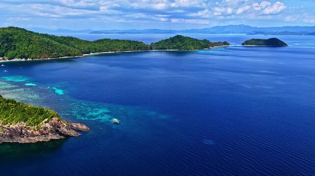 Aerial view of Port Barton Beach with lush green islands, turquoise coral reefs, and a small boat in the clear blue sea in Mimaropa, Philippines.
