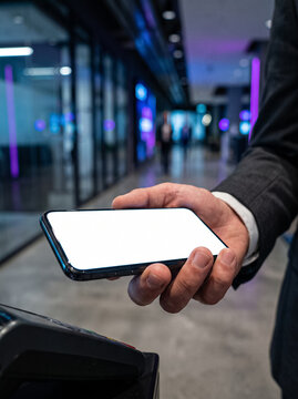 man hand bringing smartphone with white blank screen to payment terminal for contactless payment in interior