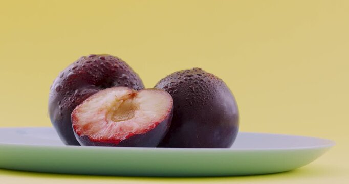 Ripe, juicy plums on a blue plate. Juicy plum cut in a half. Fruits and time of harvesting. Juicy plums sprinkled with water close up.