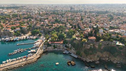 Naklejka premium Aerial view of Antalya's Kaleici old town, historic harbor, marina, turquoise water, rocky shoreline and dense urban cityscape in Turkey