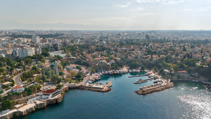 Obraz premium Aerial panorama of Antalya's Kaleici harbor with marina boats, historic old town rooftops, rocky coastline and sprawling cityscape in Turkey
