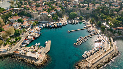Obraz premium Aerial view of Kaleici harbor in Antalya with marina boats, turquoise water, historic stone walls and red tile rooftops in Turkey