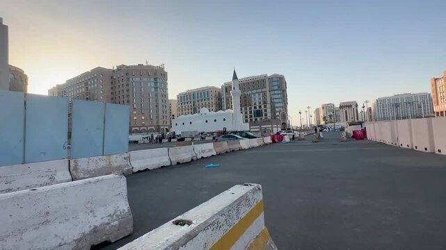Street view of the white Ali Bin Abi Talib Mosque amidst modern buildings in Medina.