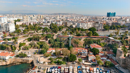 Obraz premium Aerial panorama of Antalya's Kaleici waterfront with historic red tile houses, rocky coast, harbor boats and sprawling cityscape