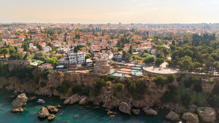 Obraz premium Aerial panorama of Antalya's Kaleici old town with Hidirlik Tower, red tile rooftops, rugged Mediterranean cliffs and turquoise sea