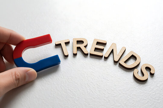 Hand holding magnet over wooden letters spelling trends on white surface