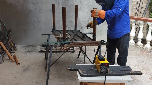 Welder holding last metal table leg in place for arc welding