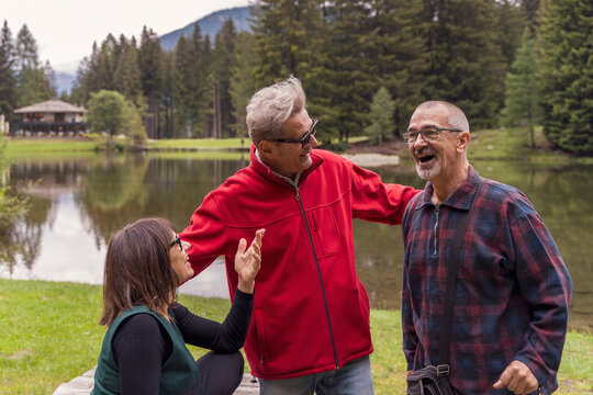 Group of happy senior friends enjoying a lively chat near a reflective lake and forest