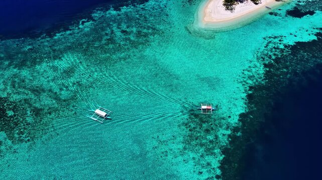 Aerial view of two traditional outrigger boats sailing through the clear turquoise waters near the sandy shores of Port Barton Beach in Mimaropa, Philippines.
