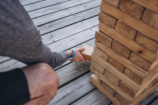 Precision Pull: A focused hand carefully slides a wooden block from a precarious tower, a moment of suspense in a game of strategy and steady nerves.