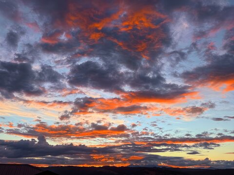 A breathtaking and dramatic sky panorama filled with fragmented, fiery orange and vermilion clouds stretching across a deep blue and violet twilight atmosphere.