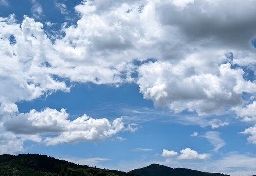 An expansive and vibrant landscape of rolling green mountain slopes standing proud under a dazzling deep blue sky dominated by dense, billowing white cumulus clouds.