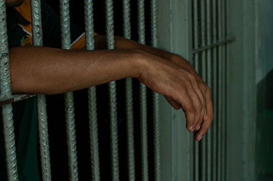 prisoner's hands behind bars with black background