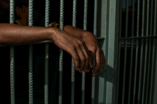 prisoner's hands behind bars with black background