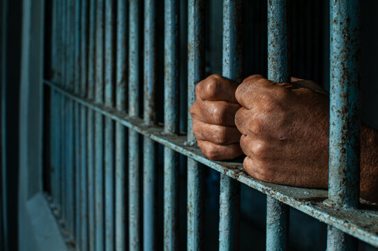 prisoner's hands behind bars with black background