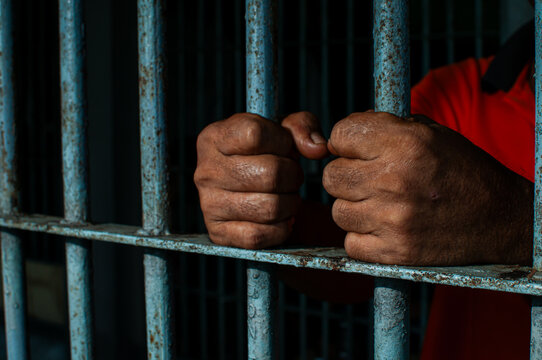 prisoner's hands behind bars with black background