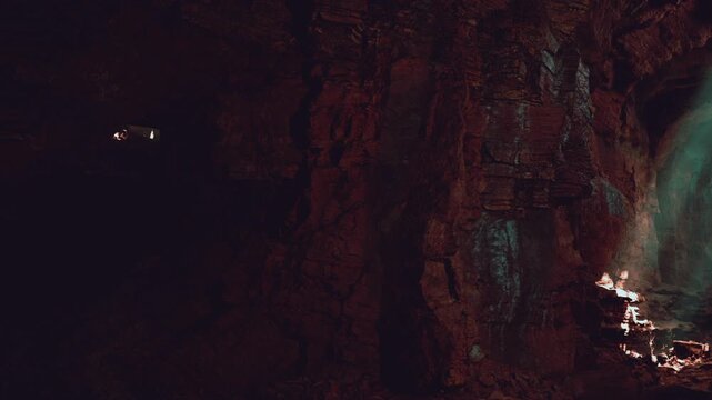 In a dark cave, light streams in from above, illuminating the rocky surfaces and creating shadows. The glow highlights the texture of the stones and the caves natural formations.
