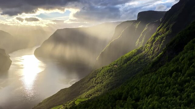Aerial view of Aurland Fjord with dramatic sunbeams breaking through clouds over steep green mountains and calm water in Aurland, Vestland, Norway.