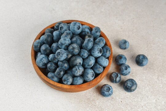 Fresh ripe blueberries in wooden bowl on a light gray textured background. Seasonal summer harvest, healthy food, natural nutrition, wholesome eating and nutritious source of vitamins and antioxidants