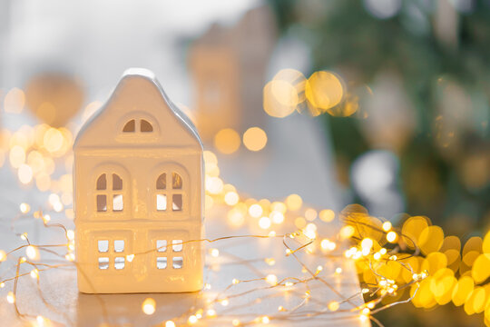 Soft Christmas scene with white ceramic house, glowing warm fairy lights and neutral winter decor. Cozy minimalist holiday background perfect for seasonal designs.