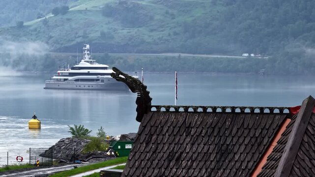 Aerial view of a luxury yacht anchored in the calm waters of the fjord near the traditional stave church architecture in Flam, Vestland, Norway.