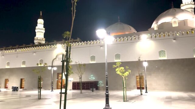 Illuminated exterior of Masjid Quba at night with glowing minarets and a plaza.