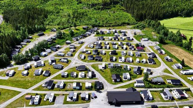 Aerial view of a large caravan park with numerous trailers and small buildings situated within a lush green forest landscape in Norway.