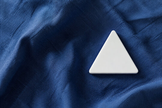 Single white equilateral triangle object on deep blue linen, calm still life for editorial concept