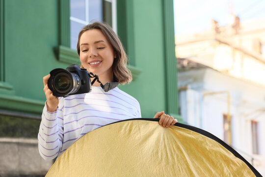 Photography hobby and creative lifestyle, young woman using professional camera and gold reflector for outdoor portrait session in city street