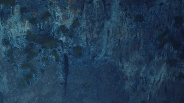 Stalactites hang from the cave ceiling in a dark and rocky area. Water drips down from the formations. The cave is located underground and shows rough textures on the walls.