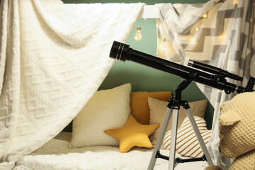 Childhood imagination and discovery, telescope in a cozy bedroom blanket fort with fairy lights for creative play and learning about astronomy at home © Pixel-Shot