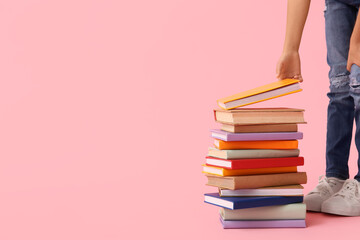 Naklejka premium Little girl with stack of colorful books on pink background