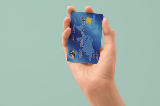 Female hand with credit card on light turquoise background, closeup