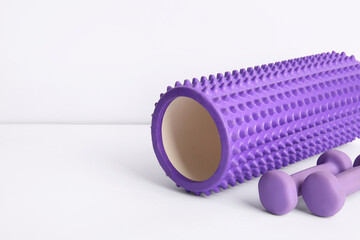 Foam roller with dumbbells on white background