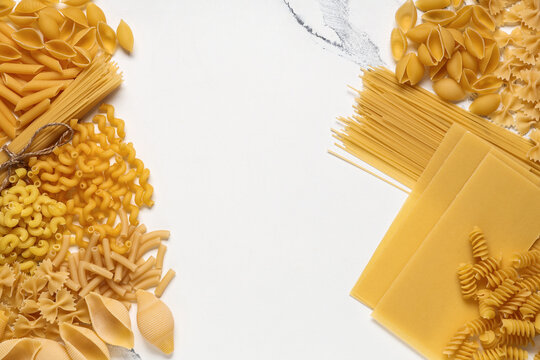 Frame made of different types of raw pasta on marble background