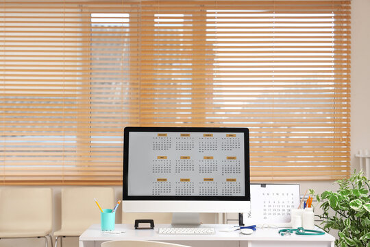 Time management and medical scheduling, computer monitor with annual calendar on desk in doctor office with stethoscope and supplies for healthcare