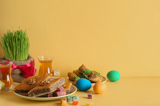 Green wheat grass, traditional sweets and tea on yellow table. Nowruz Bayram celebration