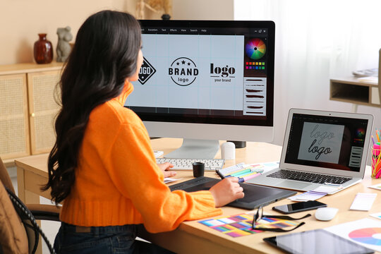 Young female graphic designer working with tablet and computer at table in office