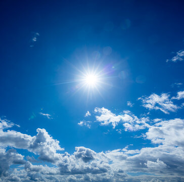 Bright sun bursting in a clear blue sky with fluffy clouds along the bottom horizon
