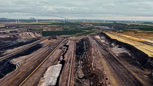 Aerial view of the vast Garzweiler surface mine with deep excavation trenches and wind turbines in the background in Juchen, North Rhine-Westphalia, Germany.