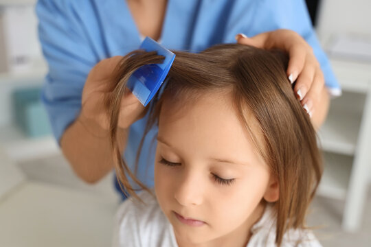 Female doctor combing little girls hair with pediculosis in clinic, closeup