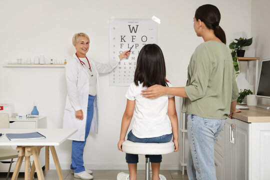 Female pediatrician checking little girls eyesight and mother in clinic