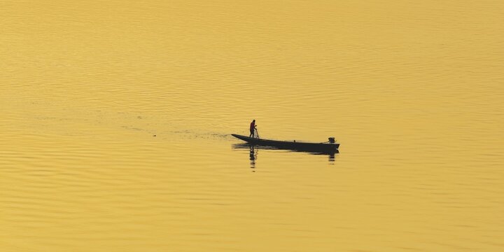 Fisherman with longtail boat (Thai: Ruea Hang Yao) at sunrise, Mekong between Thailand and Laos